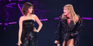 Cantoras Selena Gomez e Taylor Swift no palco rindo e segurando um microfone
