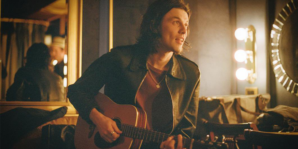 Cantor James Bay sentado em uma sala de espelhos com um violão