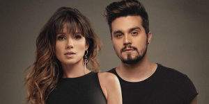 Paula Fernandes e Luan Santana usando roupas pretas em um fundo marrom