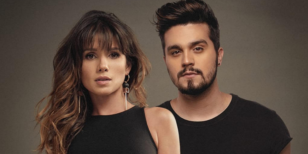Paula Fernandes e Luan Santana usando roupas pretas em um fundo marrom