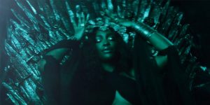 SZA sentada no Trono de Ferro de Game of Thrones com uma coroa na cabeça