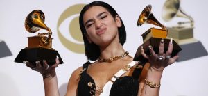 Durante a premiação dos Grammy's, Dua Lipa aparece segurando um gramofone em cada mão. Ela usa o cabelo curto e usa um vestido preto. A imagem estampa a postagem sobre as polêmicas do Grammy.