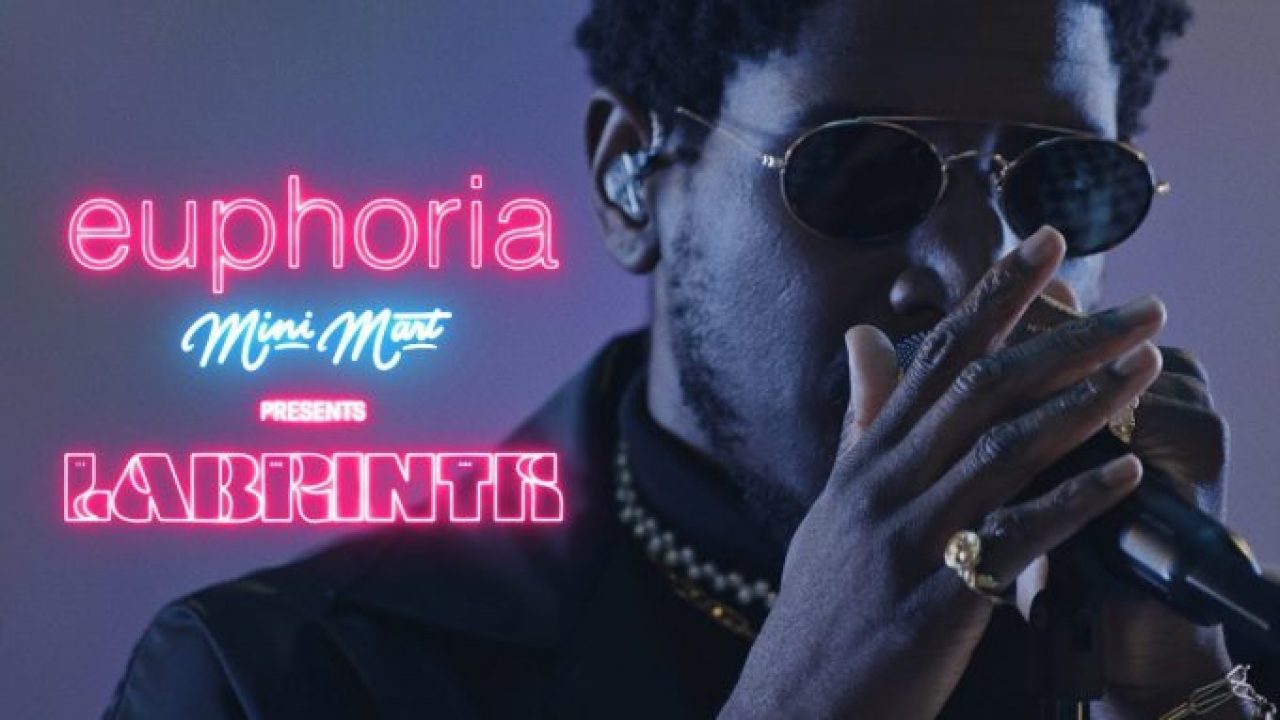 Cantor Labrinth segurando um microfone, usando um anel no dedo mindinho e óculos ovais. Ao seu lado, os escritos: euphoria - Mini Mart - PRESENTS - LABRINTH