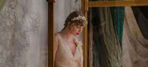 taylor swfit olhando para baixo com cabelos amarrados em coque e batom vermelho imagem é de divulgação do clipe de willow single do album evermore