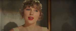 taylor swift no videoclipe de willow primeiro single do album evermore ela olha para a frente vestindo tiara e batom vermelho