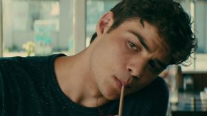 peter kavinsky, personagem da netflix que ganhou uma playlist no spotify, de blusa preta tomando um milk shake