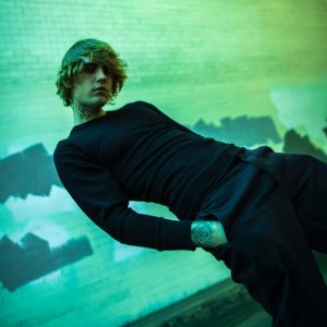 A imagem apresenta Justin Bieber em pé na diagonal. A fotografia está em um tom esverdeado e Justin está vestindo calças pretas e camisa da mesma cor. Com as mãos no bolso, Bieber olha para frente, com a cabeça um pouco abaixada. A imagem destaca a Deluxe Version do Justice.