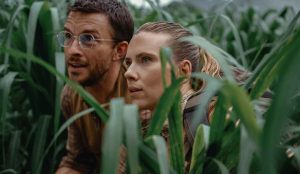 Zora Bennett (Scarlett Johansson) e personagem de Jonathan Bailey escondidos entre folhagens em cena tensa de 'Jurassic World: Recomeço'.