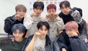 A imagem mostra os sete integrantes do ALL(H)OURS reunidos em um momento descontraído. Kunho, Youmin, Xayden, Minje, Masami, Hyunbin e ON:N aparecem fazendo um gesto fofo com as mãos