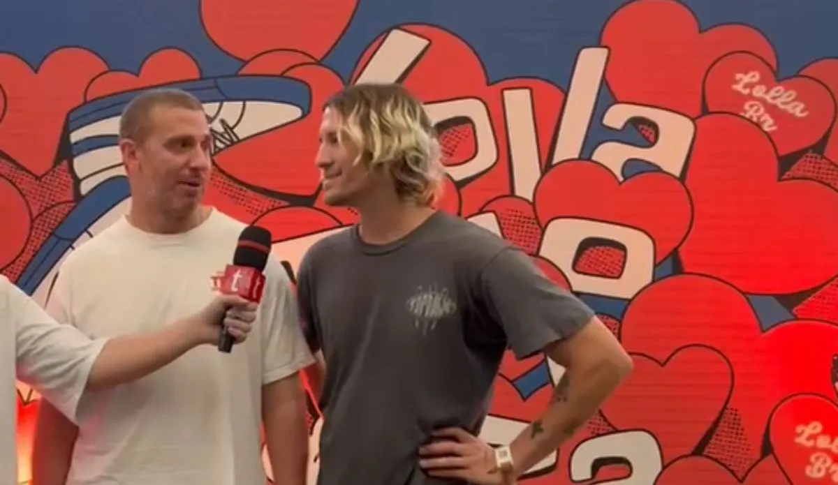 A imagem mostra os integrantes do duo Neil Frances sendo entrevistados durante o Lollapalooza Brasil 2025. O fundo apresenta um design vibrante, com corações vermelhos e o nome "Lollapalooza" estilizado