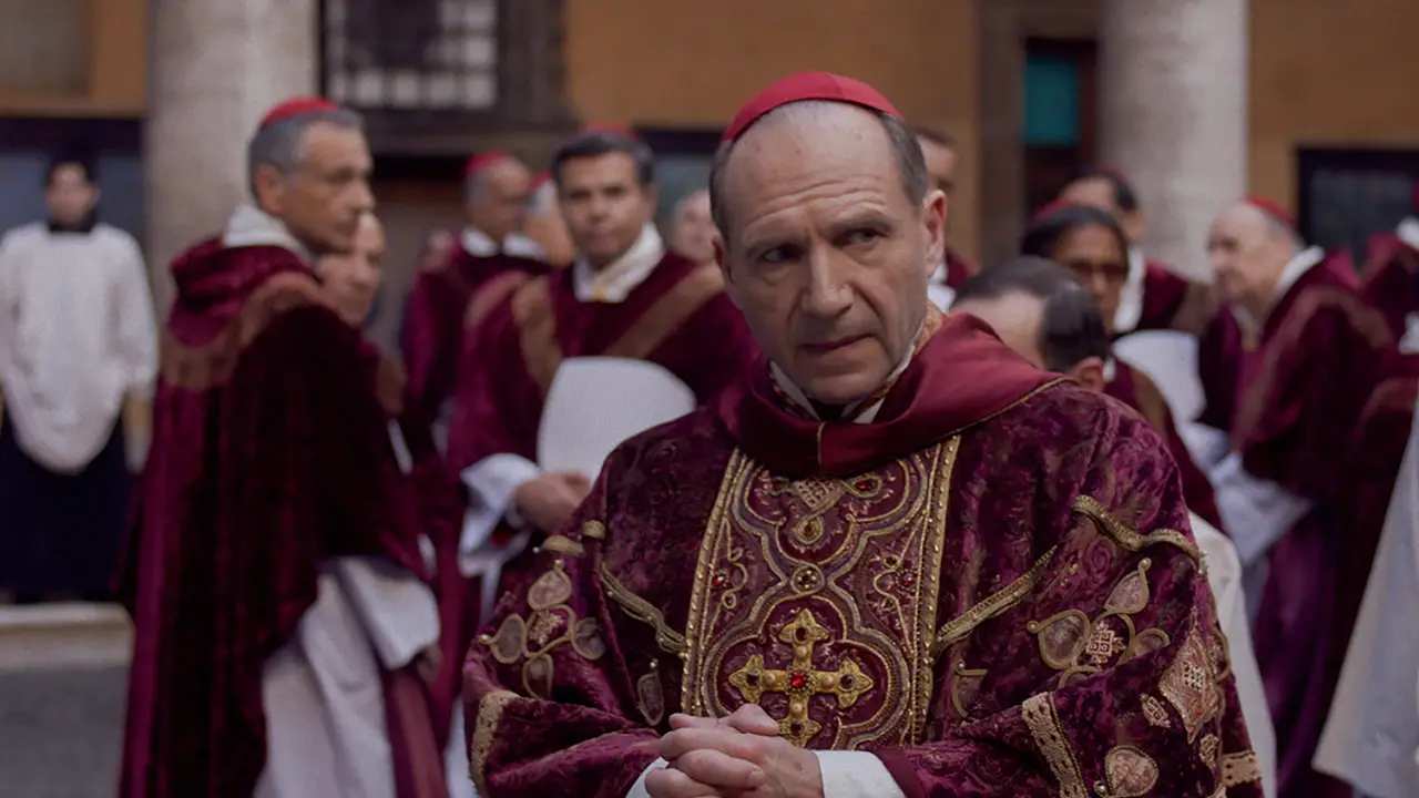Cena do filme "Conclave" com Ralph Fiennes caracterizado como cardeal, cercado por outros religiosos vestindo trajes litúrgicos