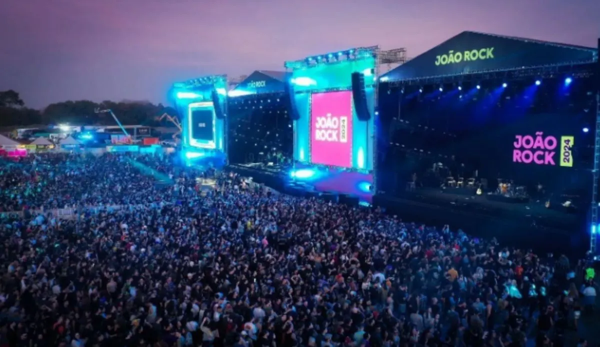 Palco principal do festival João Rock durante a edição de 2024, com uma multidão reunida em frente ao palco iluminado em tons de azul e roxo, ao entardecer