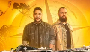 Imagem promocional do Navio temático Jorge e Mateus – 20 Anos. A dupla sertaneja aparece em destaque, com Jorge à esquerda usando uma jaqueta jeans e Mateus à direita com camisa estampada e colar. Ao fundo, um fundo dourado com bússola estilizada e a frase “A nossa história é de arrepiar!”. Na parte inferior, aparece o cruzeiro MSC Preziosa, navio onde acontecerá o evento em 2026