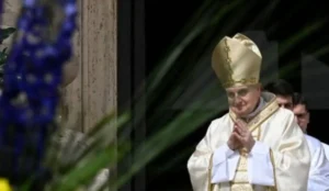 Papa Francisco com vestes litúrgicas brancas e mitra dourada, de mãos postas em oração, durante cerimônia