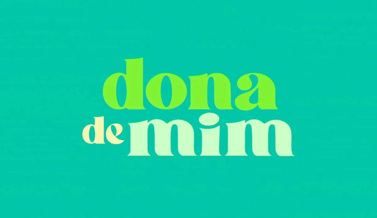 A imagem apresenta a frase "dona de mim" em uma fonte estilizada. As palavras estão exibidas em um fundo azul-petróleo. A palavra "dona" está em verde claro, "de" em pêsseg claro e "mim" em menta clara.