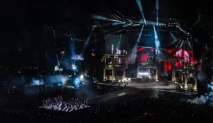 Show de Lady Gaga em grande palco montado na orla de Copacabana, com estrutura grandiosa, iluminação intensa e dançarinos performando diante de uma multidão.