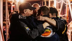 Integrantes do Coldplay se abraçam nos bastidores de um show, usando figurinos com elementos gráficos