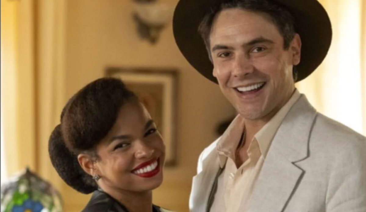 Sergio Guizé e Jeniffer Nascimento em cena da novela “Êta Mundo Melhor!”, da TV Globo. Os personagens aparecem sorridentes, vestidos com figurinos de época, em ambiente interno iluminado.