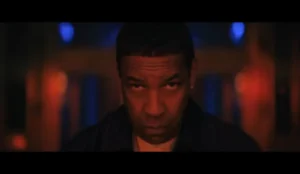 "Denzel Washington encara a câmera em cena do filme Highest 2 Lowest, com iluminação dramática em tons vermelhos e azuis