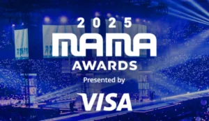 Logo do MAMA Awards 2025 sobre uma arena iluminada em azul, com palco e público ao fundo. Evento é patrocinado pela Visa.