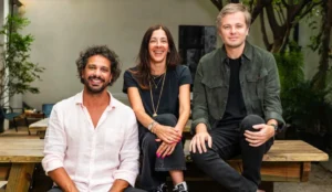Guilherme Teixeira, Leca Guimarães e Tiago Maia, fundadores da SUPER SOUNDS, sentados sorrindo em um ambiente externo com mesas de madeira e vegetação ao fundo