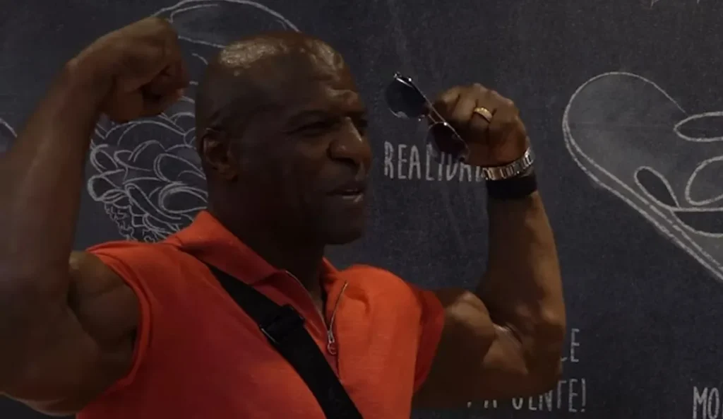 Terry Crews posa sorridente e faz pose de fisiculturista, com os braços flexionados, durante visita ao Mercado Municipal de São Paulo