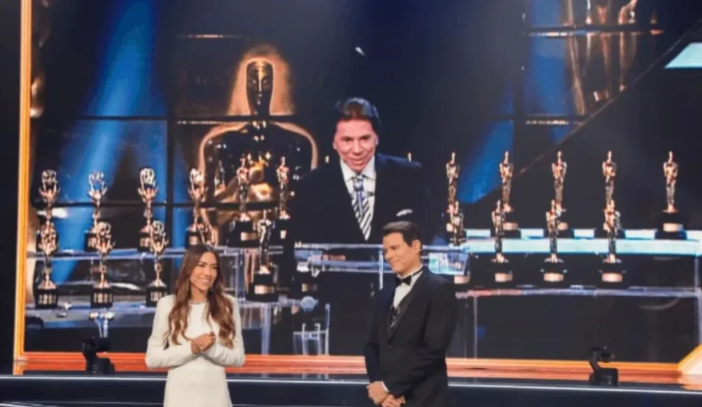 Patricia Abravanel e Celso Portiolli no palco do Troféu Imprensa 2025, com troféus ao fundo e uma grande tela exibindo Silvio Santos em imagem de arquivo, durante homenagem ao apresentador.