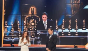 Patricia Abravanel e Celso Portiolli no palco do Troféu Imprensa 2025, com troféus ao fundo e uma grande tela exibindo Silvio Santos em imagem de arquivo, durante homenagem ao apresentador.