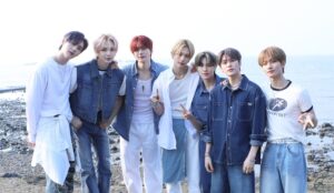 Sete integrantes do EPEX posam lado a lado à beira-mar, em um cenário natural com pedras e mar ao fundo. Eles usam looks em tons de azul, branco e jeans, transmitindo um conceito leve e juvenil. Todos estão sorrindo ou fazendo gestos com as mãos, em clima descontraído.