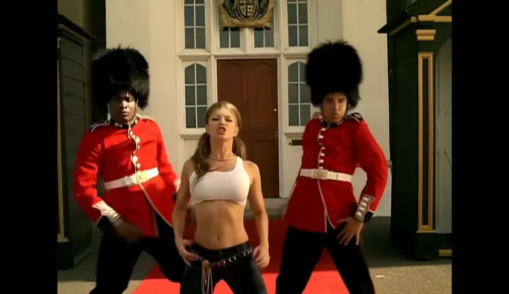 Fergie no clipe original de “London Bridge”, de 2006, dançando ao lado de dois guardas britânicos com uniformes vermelhos e chapéus de pele, em frente a um prédio com arquitetura clássica em Londres.