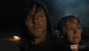 Daryl (Norman Reedus) e Carol (Melissa McBride) encaram o horizonte em cena sombria da 3ª temporada de The Walking Dead: Daryl Dixon; ambos têm expressão séria e cabelos ao vento, sob luz baixa.