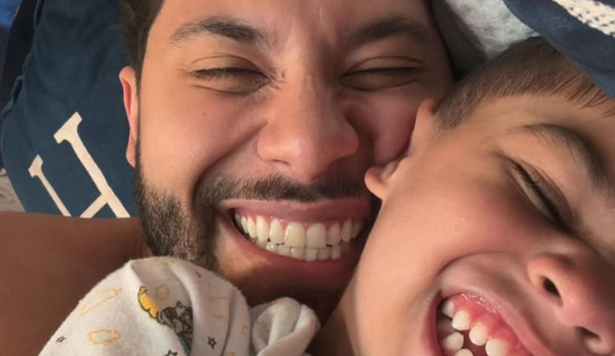Murilo Huff e seu filho Léo sorrindo abraçados em uma selfie. Ambos estão com os olhos fechados e expressam alegria e afeto no momento.