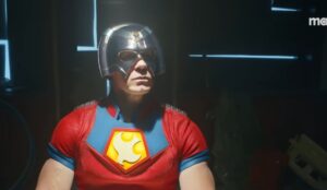 Cena da série 'Pacificador' mostrando John Cena vestido como o personagem Christopher Smith, com o uniforme vermelho e azul característico e capacete prateado, em um ambiente escuro iluminado por luzes de fundo.