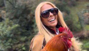 Adriane Galisteu posa sorridente segurando um galo durante divulgação de A Fazenda 17, reality show da Record.