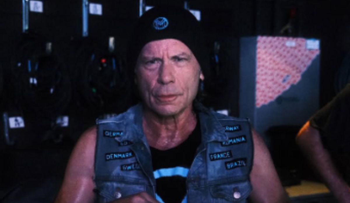 Bruce Dickinson, vocalista do Iron Maiden, usando gorro preto e colete jeans com patches de países em foto de bastidores de sua turnê "The Mandrack Projetc"; cantor se apresentou no The Town 2025.