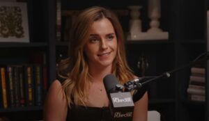 Emma Watson durante entrevista ao podcast “On Purpose With Jay Shetty”, falando em frente a um microfone com estante de livros ao fundo.