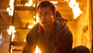 Cena de O Sobrevivente mostra Glen Powell em ambiente em chamas, com expressão intensa.