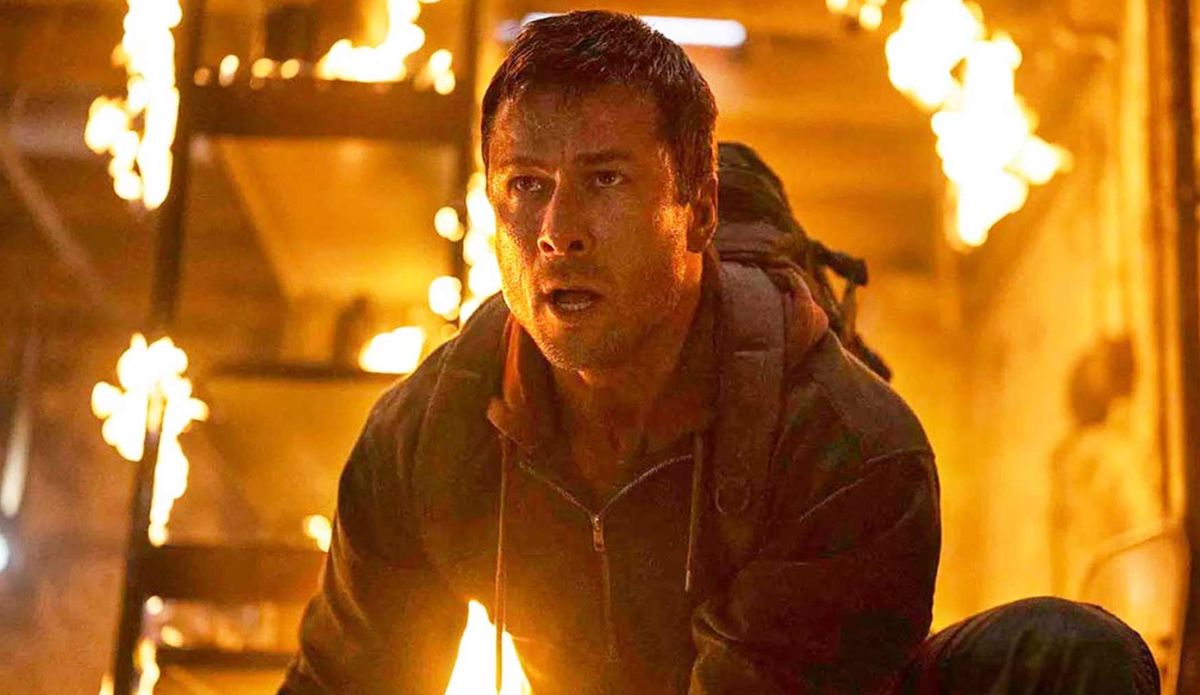 Cena de O Sobrevivente mostra Glen Powell em ambiente em chamas, com expressão intensa.