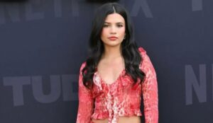 Nikki Rodriguez em evento da Netflix, com blusa vermelha estampada e cabelos soltos; atriz está no centro da polêmica sobre sua idade.