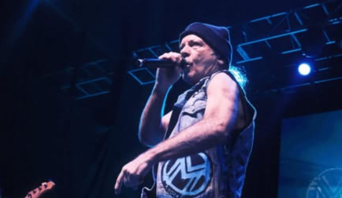 Bruce Dickinson canta no palco, vestindo colete jeans e gorro preto, segurando microfone sob luzes azuis durante apresentação ao vivo; confira a provável setlist do músico que se apresenta no The Town 2025