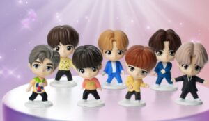 Brinquedos TinyTAN do BTS no McDonald’s: bonecos colecionáveis dos sete integrantes em versão chibi, com roupas coloridas e estilosas, expostos em um fundo lilás com brilho.