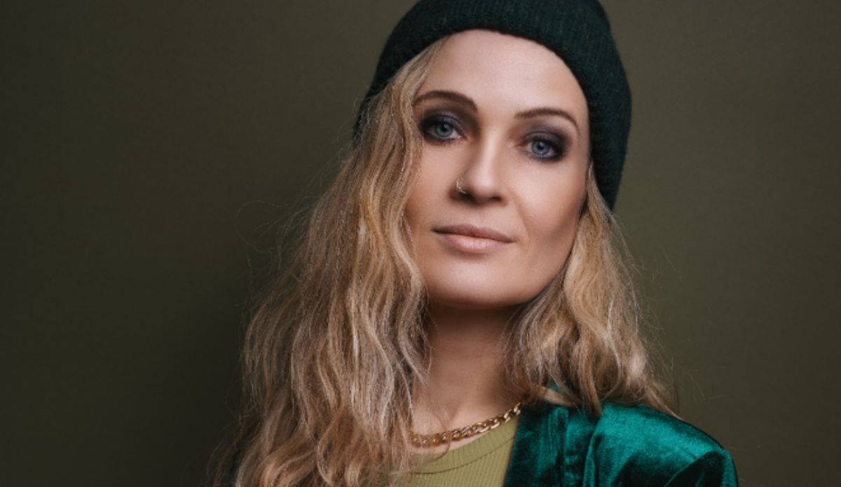 Retrato de Anika Nilles, nova baterista do Rush, usando gorro escuro e jaqueta verde. A musicista alemã foi anunciada como integrante da turnê de retorno da banda em 2026.
