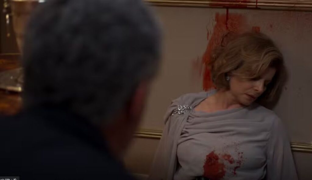 Cena do remake de “Vale Tudo” mostra o momento em que Odete Roitman é encontrada sem vida, após ser baleada, encostada à parede com manchas de sangue ao fundo.