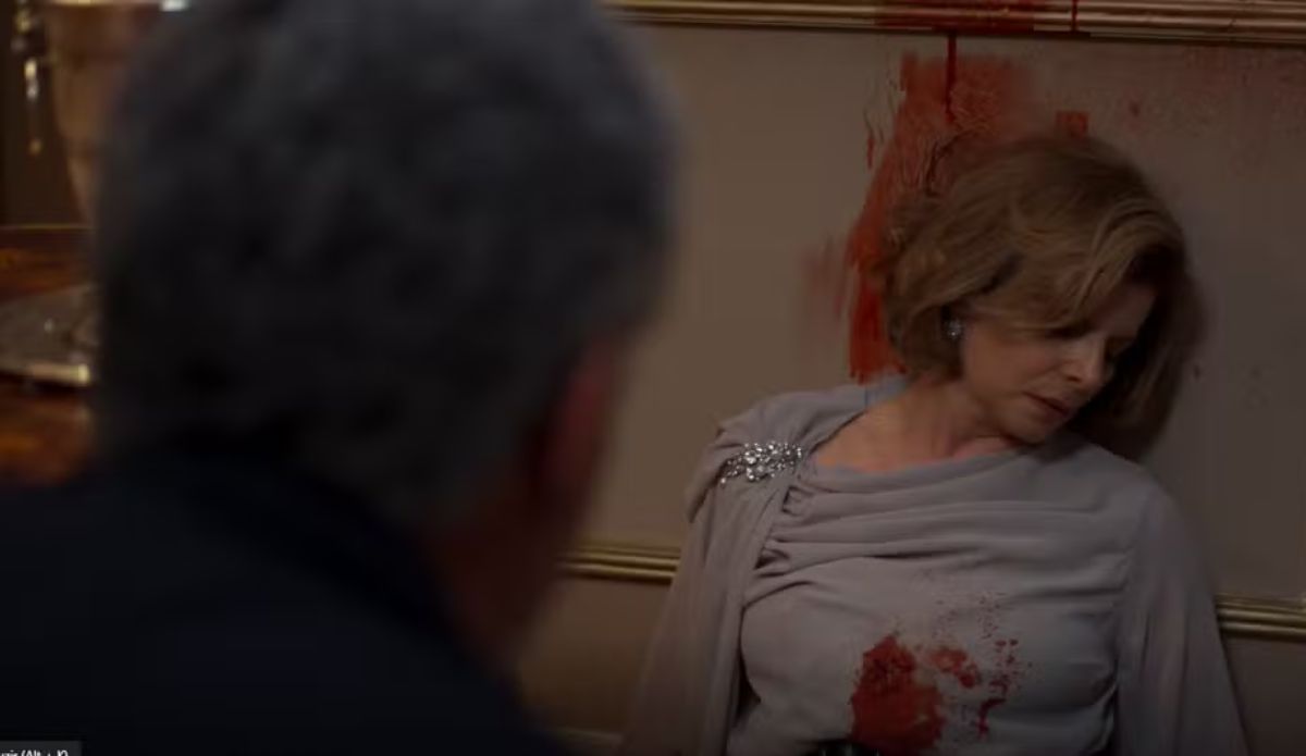 Cena do remake de “Vale Tudo” mostra o momento em que Odete Roitman é encontrada sem vida, após ser baleada, encostada à parede com manchas de sangue ao fundo.