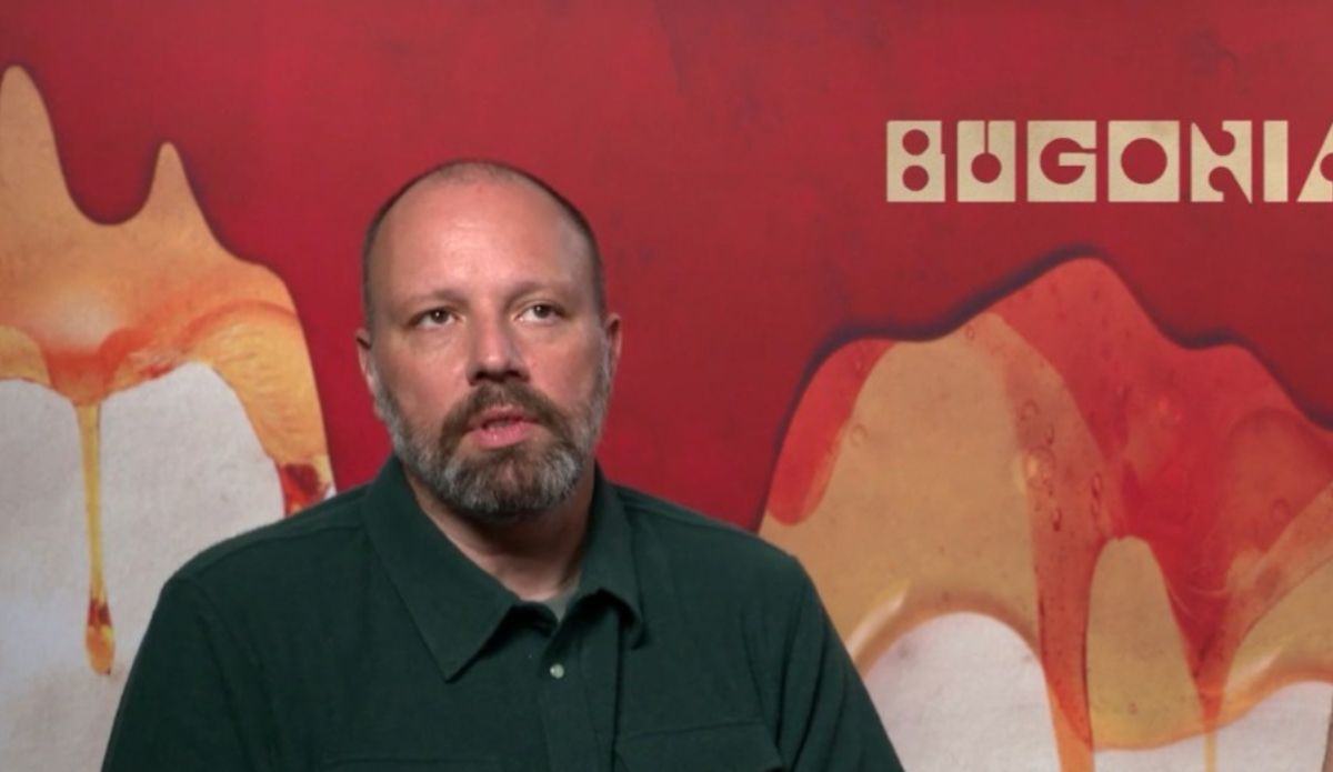 Yorgos Lanthimos durante entrevista de divulgação do filme “Bugonia”, com pôster vermelho ao fundo