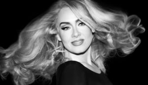 Adele em retrato em preto e branco, com cabelos soltos ao vento, imagem promocional da cantora que fará estreia como atriz no cinema.