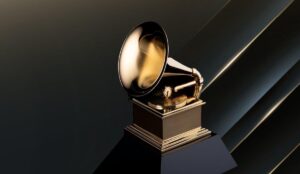 Imagem do troféu dourado do Grammy, em formato de gramofone, sobre uma base preta, com fundo escuro e detalhes metálicos iluminados.