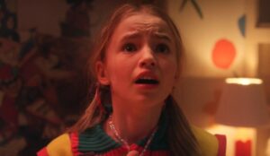 Holly Wheeler, assustada, olha para cima em uma cena iluminada em tons quentes da 5ª temporada de Stranger Things.
