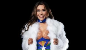 Silvânia Aquino posa sorridente com um figurino colorido inspirado na bandeira do Brasil e casaco branco de pelúcia, em fundo preto.