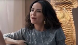 Cena de Três Graças mostra Zenilda sentada, usando blusa cinza brilhante, em momento de tensão na novela.